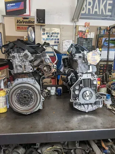 Two car engines on a metal workbench in a garage setting.