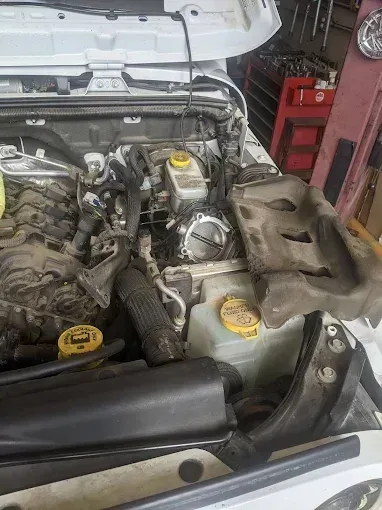 Open Jeep engine bay with components exposed; white vehicle, black air intake.