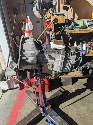 Transmission on a red lift in a garage, secured by a blue strap.