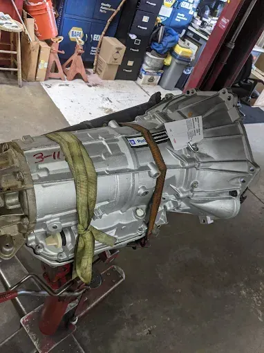 Silver transmission strapped on a red stand inside a garage with tools and boxes.