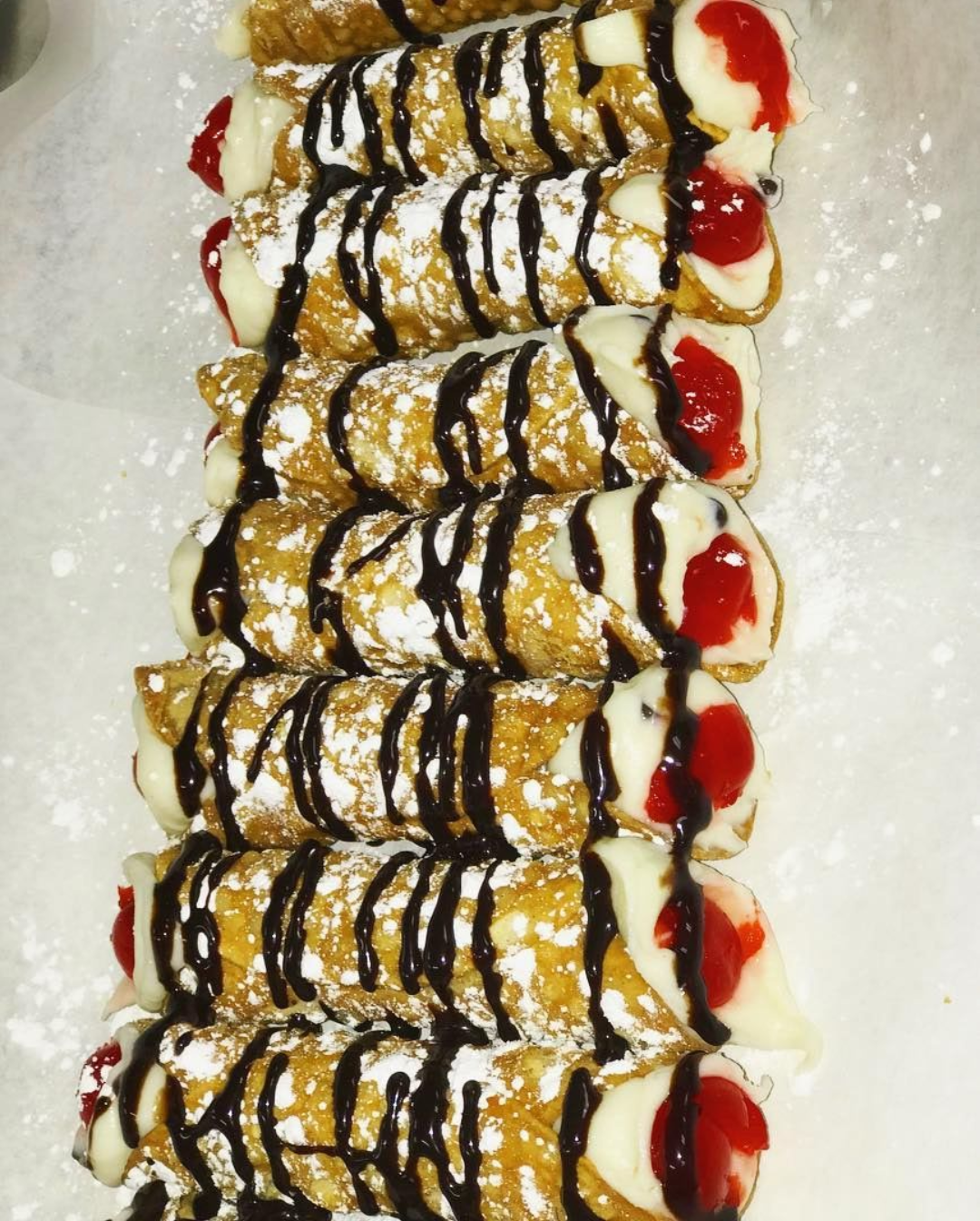Cannoli pastries drizzled with chocolate and dusted with powdered sugar.