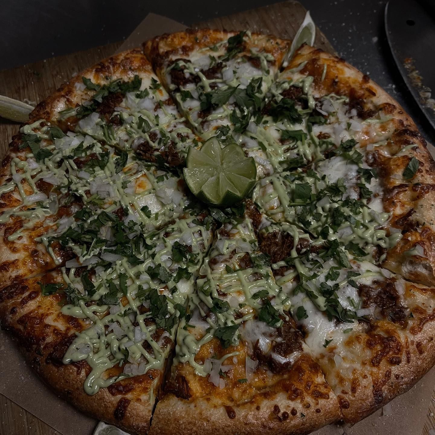 Pizza with toppings, cilantro, sauce, and a lime slice on a wooden surface.