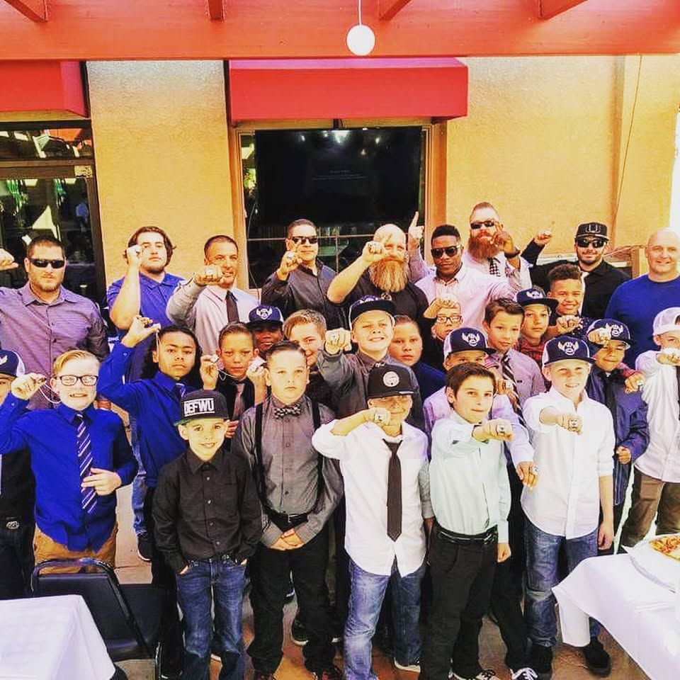 Group of men and boys outside, raising fists. Some wear suits and hats.