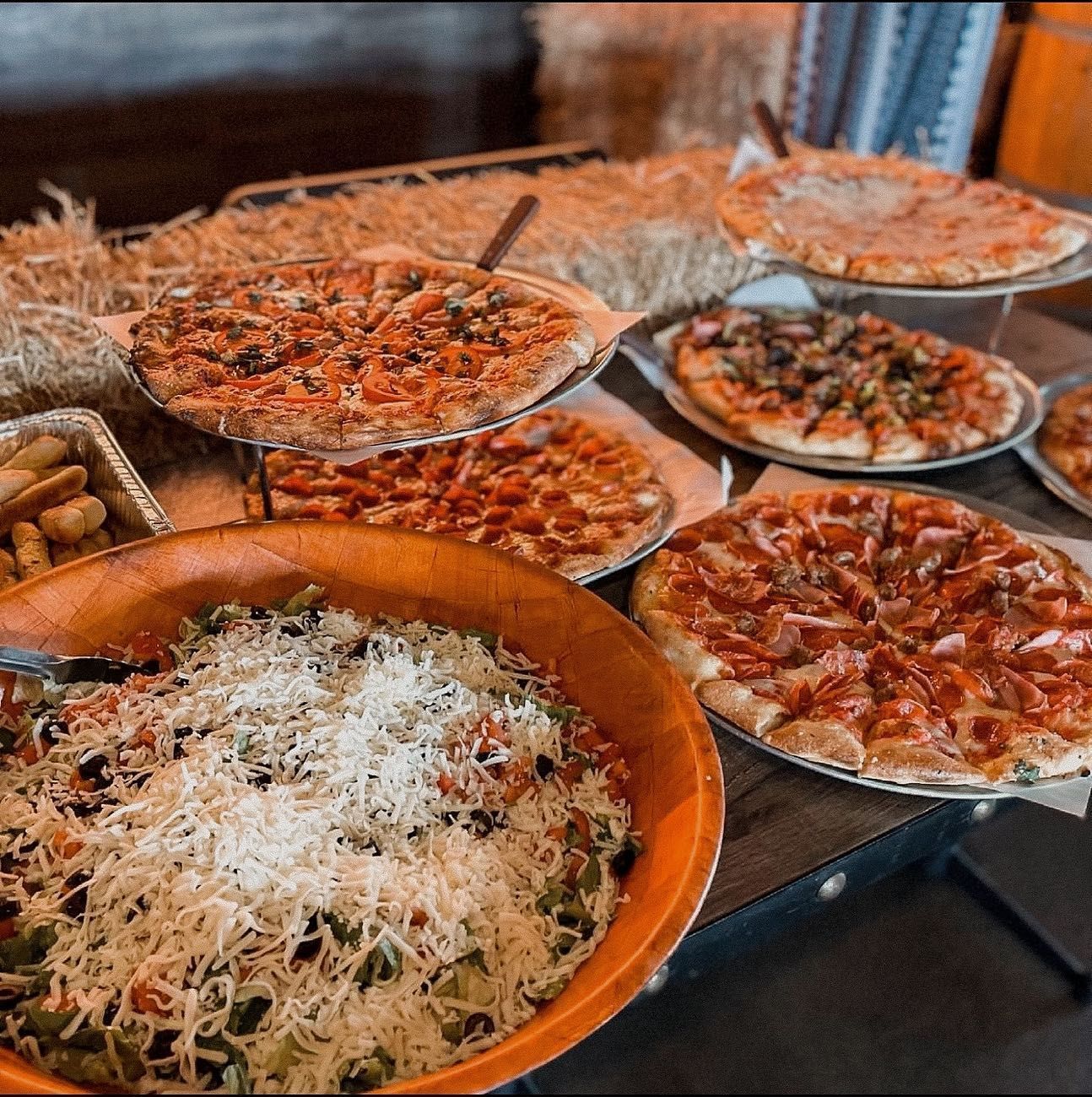Pizzas and pasta buffet on a table with hay bales in the background. Close up of food with cheese.