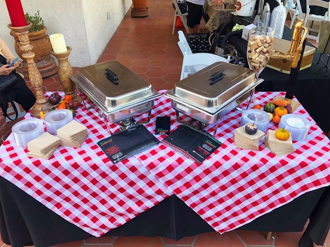 A display table with red-and-white checkered cloth, stainless steel food warmers, candles, and printed menus.