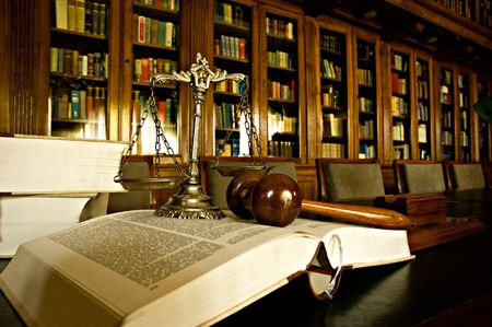 Scales of justice, gavel, and open law book on a desk in a library.