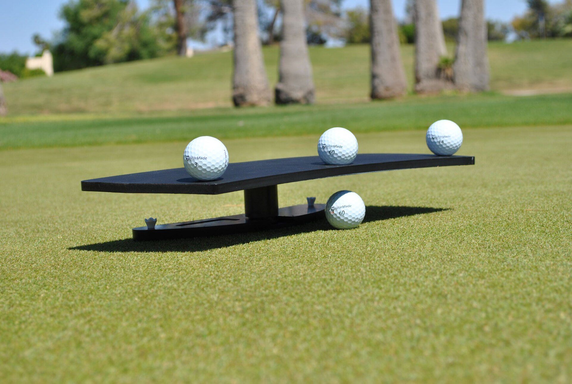 A black golf ball alignment tool with four golf balls on a green course.