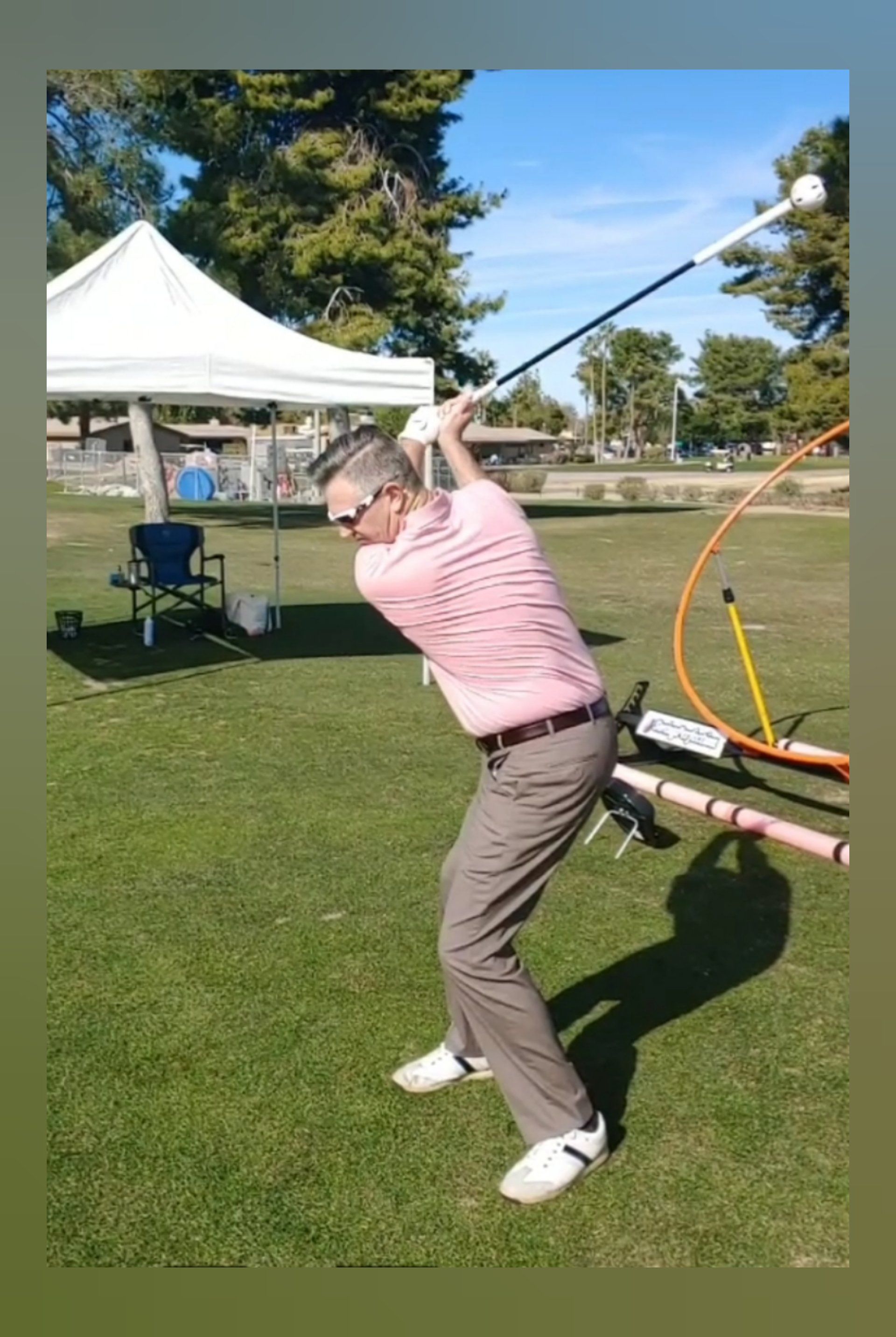Man in pink shirt swinging golf club on green grass.