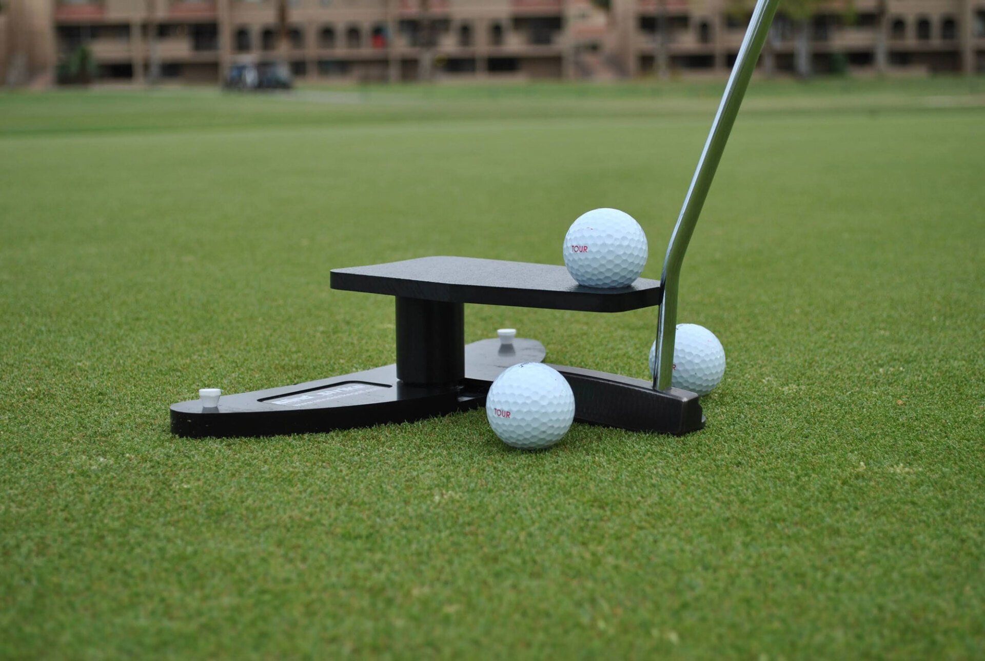 Golf putter with three golf balls on a putting green.