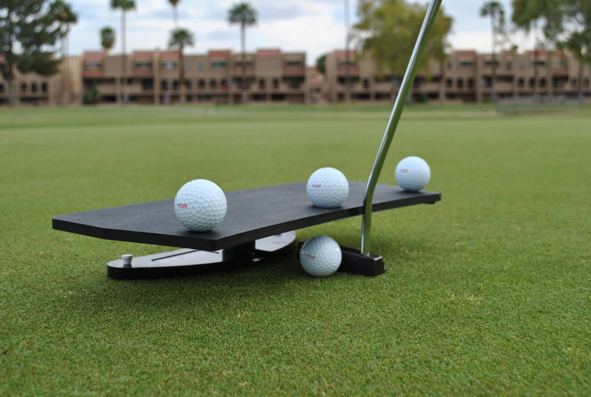 A golf putting aid with golf balls on a green, with a metal rod for alignment.