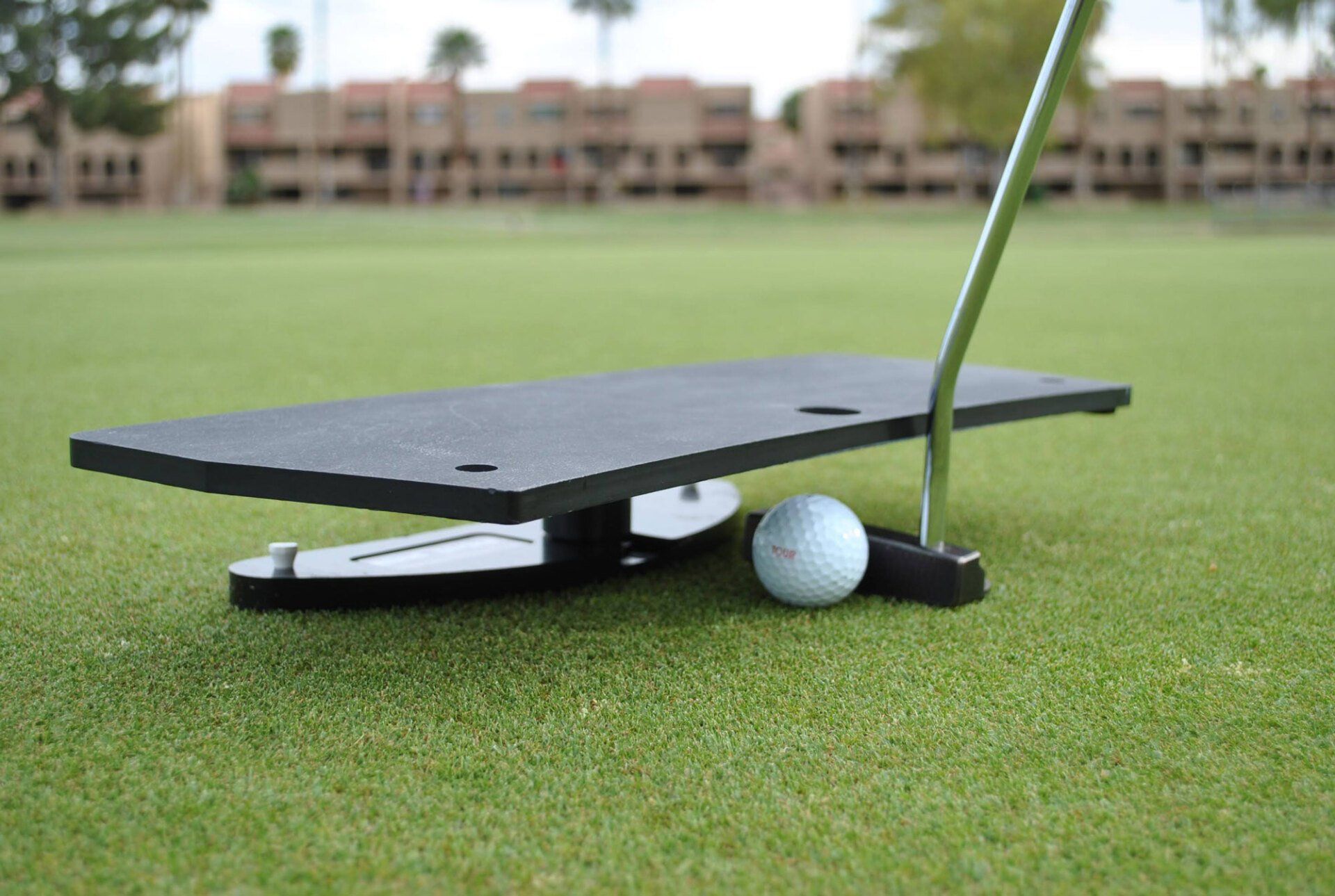 A golf putting aid on green grass with a golf ball and putter.