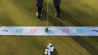 Golfer putting on a putting green, using a training aid with alignment markings.