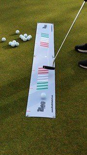 Golfer practicing putting on green with a white alignment mat, balls, and putter.