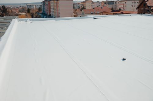 Snow-covered flat rooftop with a small vent and buildings in the background