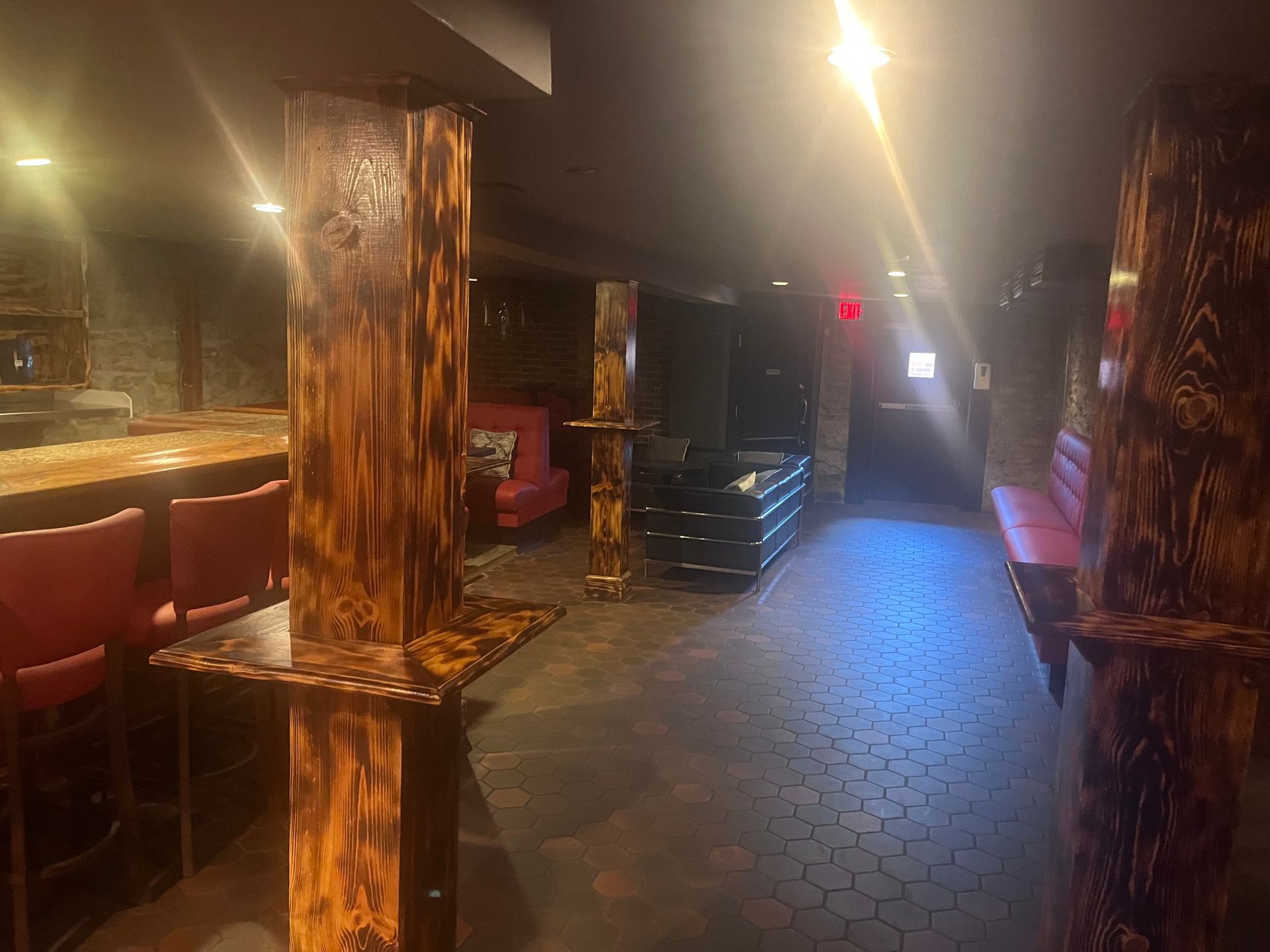 Interior of a bar with red seating, a bar, and textured wooden support beams.