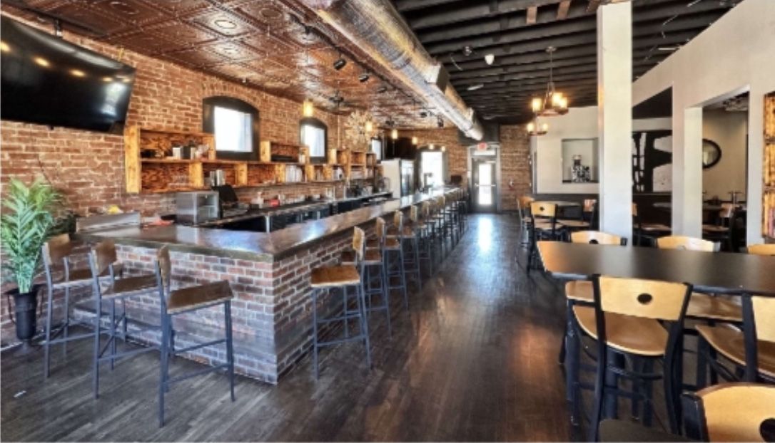 Interior of a bar and restaurant with brick walls, a bar, tables, and chairs.