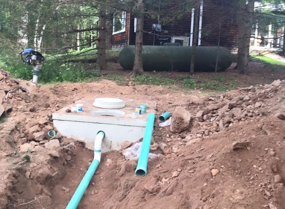 A septic tank is being installed in the dirt in front of a house.