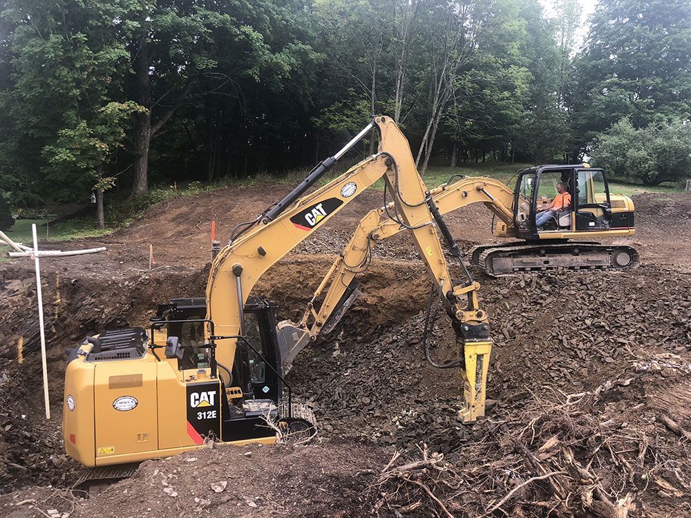 A couple of excavators are digging a hole in the dirt.