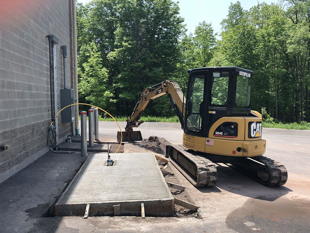 A yellow cat excavator is working on a concrete slab.
