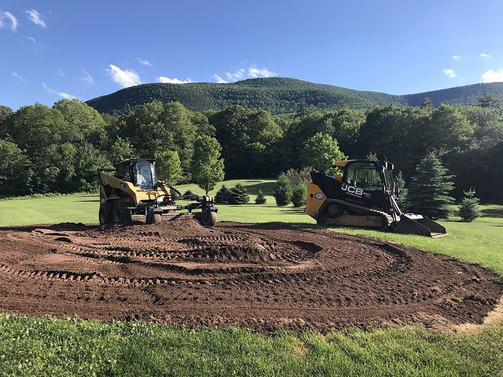 Two bulldozers are working on a dirt field with mountains in the background.