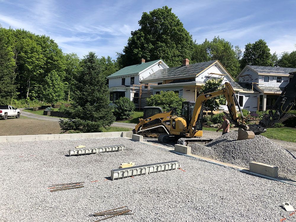 An excavator is sitting on top of a gravel lot in front of a house.