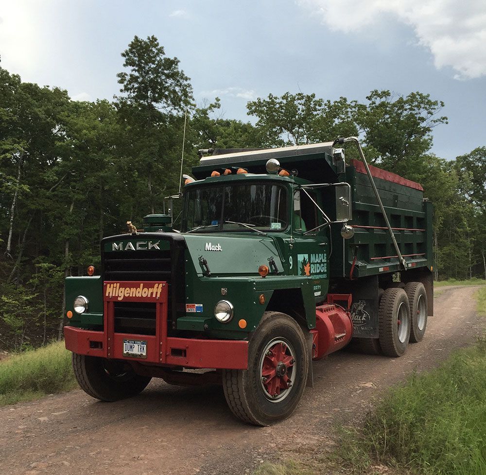 A mack dump truck is driving down a dirt road