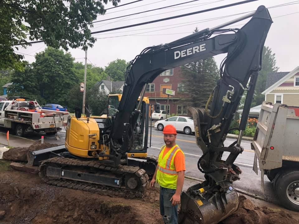 A man is standing in front of a deere excavator.