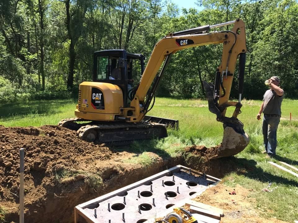 A man is standing next to an excavator digging a hole in the ground.