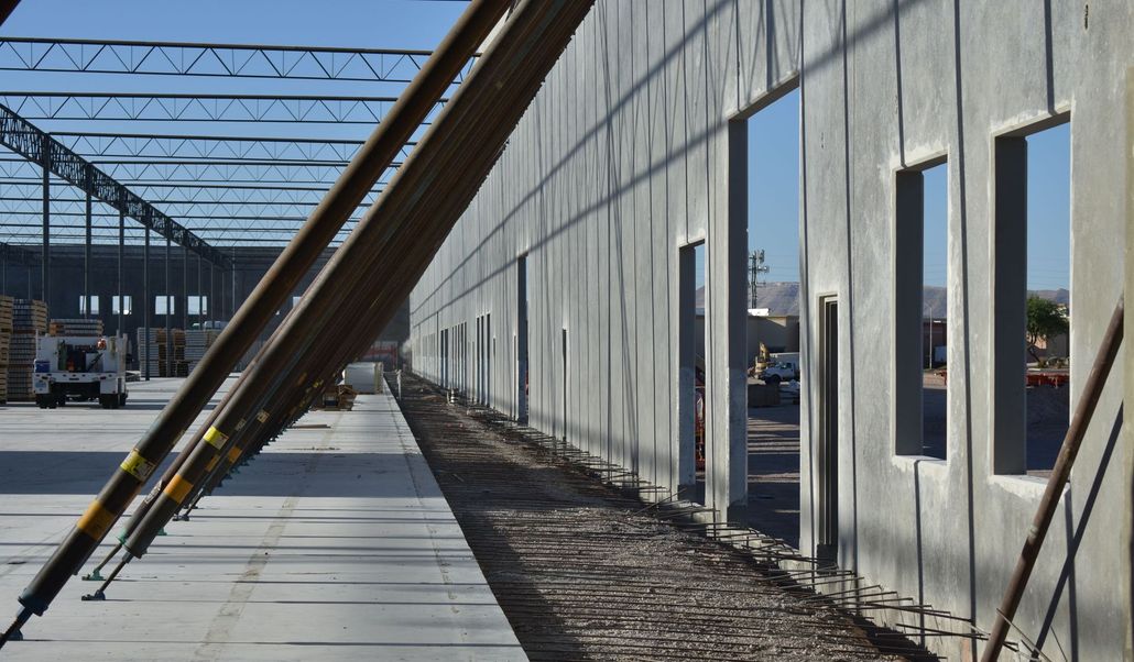 Construction site with concrete wall, steel beams, and open window openings under a metal roof frame