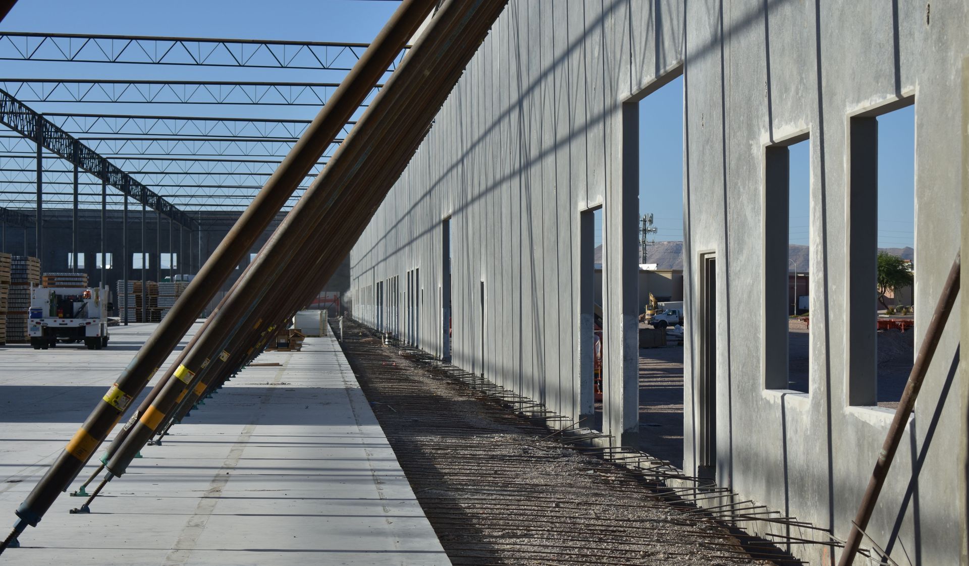Construction site with concrete wall, steel beams, and open window openings under a metal roof frame