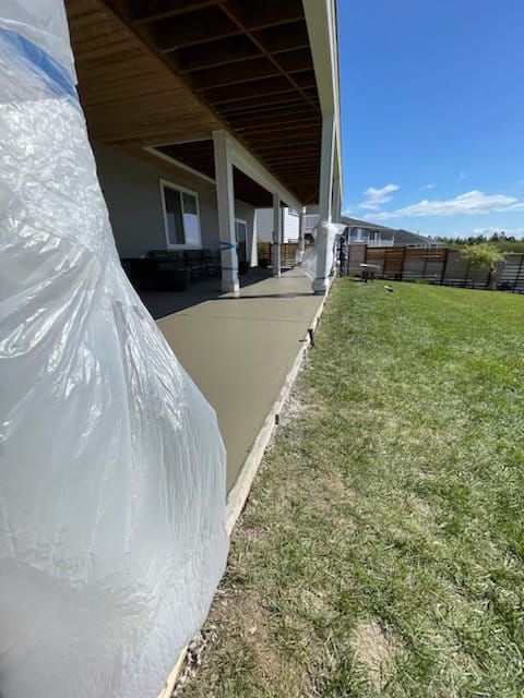 Covered patio beside grassy yard, with a white wrapped object in the foreground and blue sky beyond