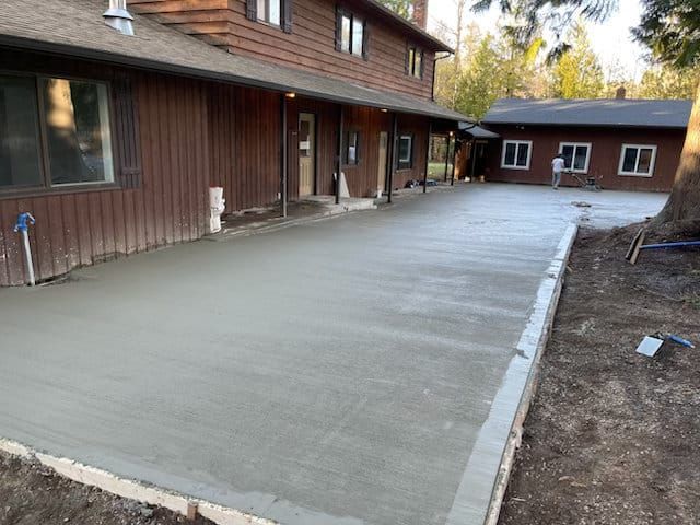 Freshly poured concrete walkway beside a brown wooden house and garage in a yard