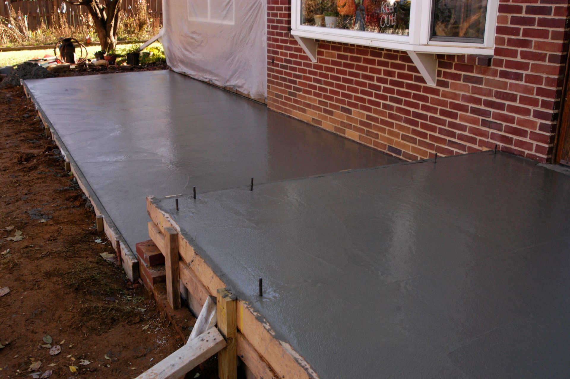 Fresh concrete sidewalk along a brick house foundation with exposed stakes and dirt edges