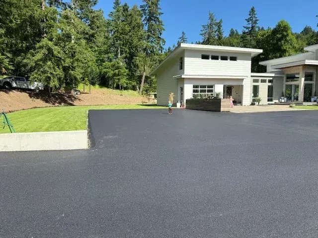 Black asphalt driveway in front of a modern white house with a person walking on the driveway.