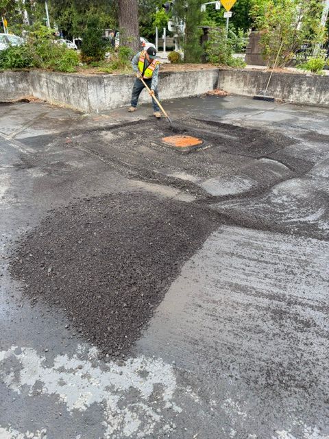 Worker patching a pothole in a parking lot with fresh black asphalt