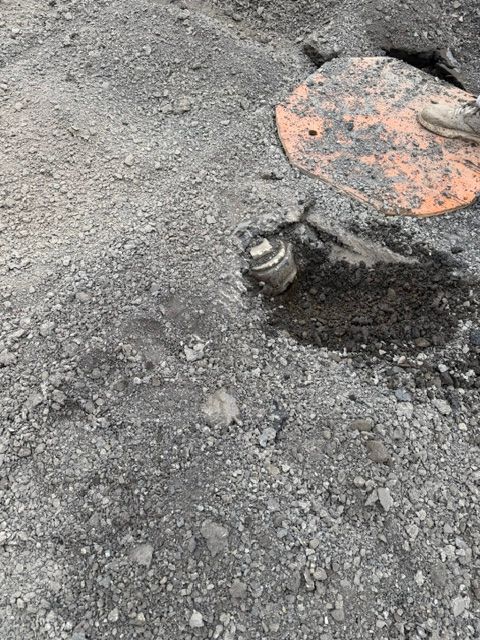 Pothole in rough asphalt with a metal utility cover