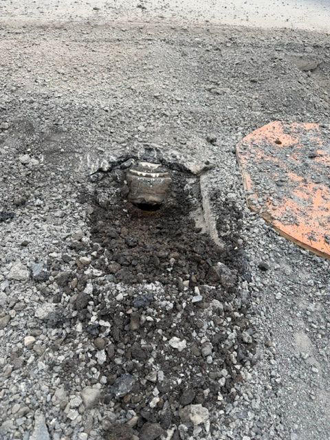 Pothole in rough asphalt with a metal utility cover