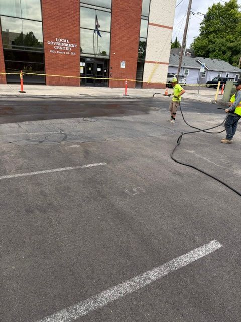 Workers paving an asphalt lot beside a brick building