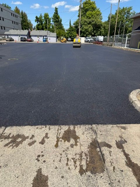 Parking lot with fresh black asphalt and a small yellow roller under a blue sky
