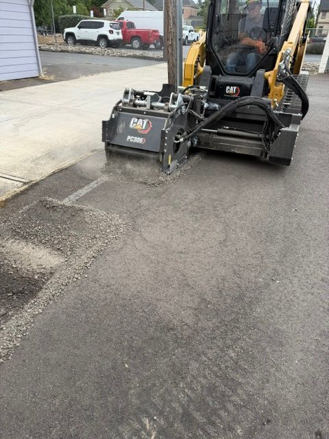 Compact loader removing pavement near a building entrance, with a worker seated inside.