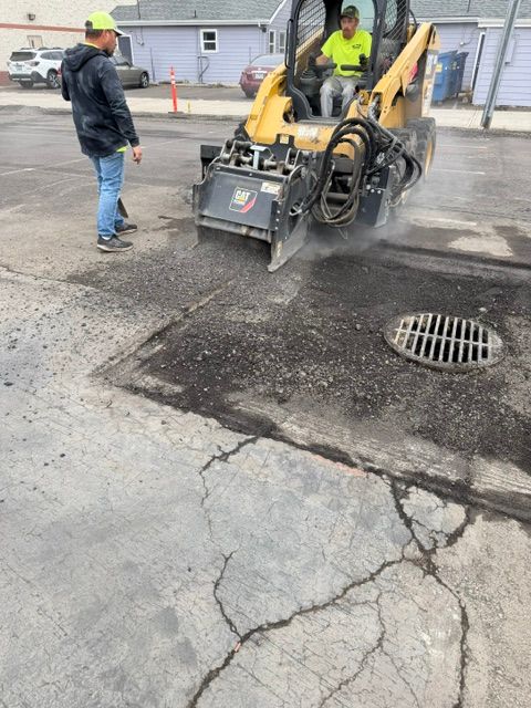 Crew repairs cracked road with a yellow paving machine near a storm drain.