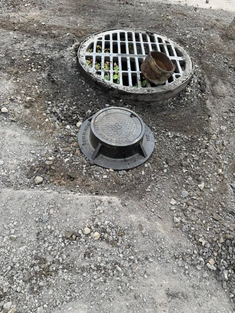 Roadside drain grate beside a round manhole cover.
