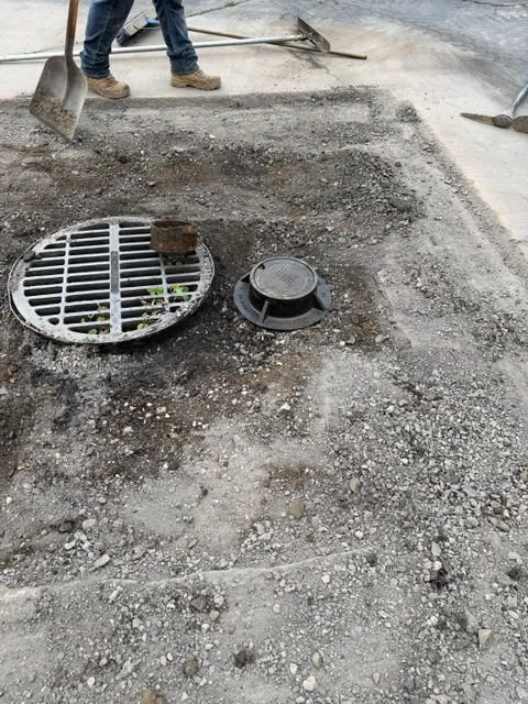 Construction workers paving around a storm drain and manhole on a gravel road