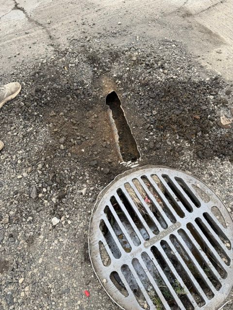 Storm drain grate with a cracked pavement and narrow drainage opening beside it