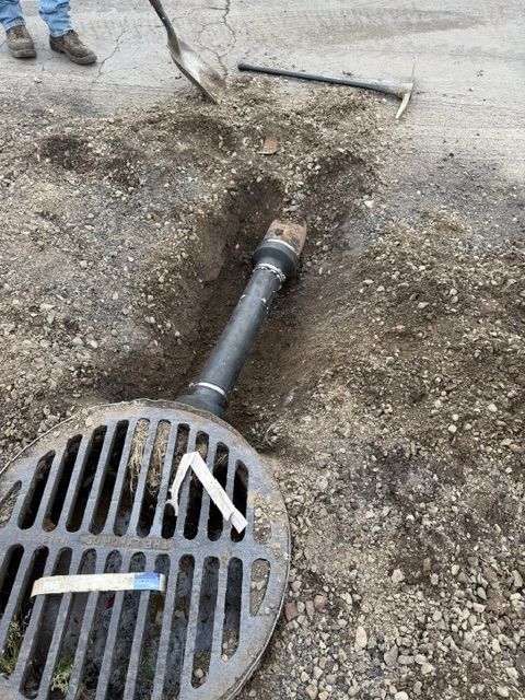 Storm drain grate with a detached pipe in a dug-up gravel roadway