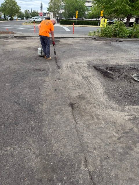 Worker in orange shirt patching a cracked asphalt parking lot