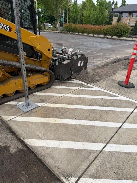 Yellow construction machine on a striped pedestrian crossing beside orange cones and a curb.