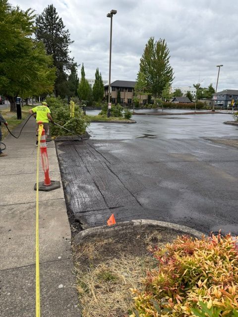 Worker installing curb along wet asphalt parking lot with cones and tape near landscaped area