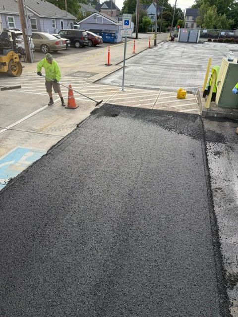 Roadwork scene with fresh black asphalt patch, worker in neon vest