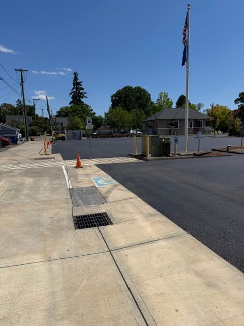 Concrete sidewalk leading to a small gated entrance with an American flag and parking lot under a clear blue sky